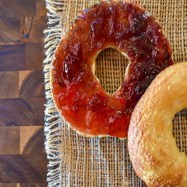 Two Bagel Nosh bagels, one plain and one with a thick layer of glistening red jam, on burlap.