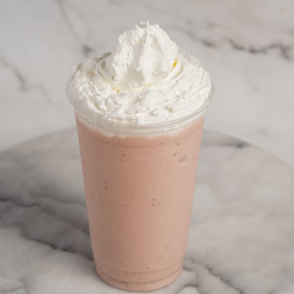 A pink smoothie topped with a generous swirl of white whipped cream in a clear plastic cup.