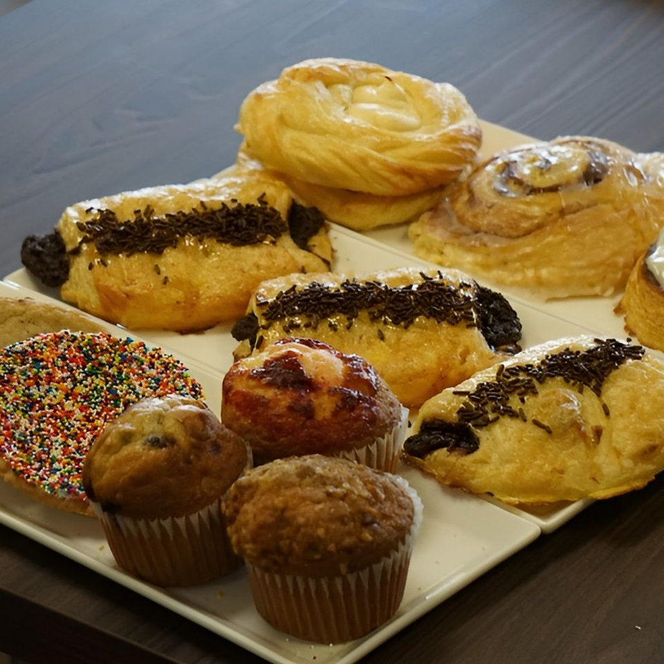 A white tray filled with various Bagel Nosh pastries, muffins, and a sprinkle-covered cookie.