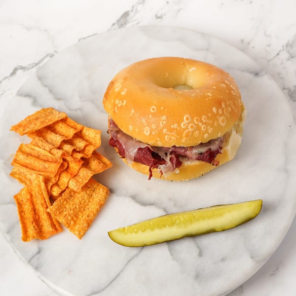 Bagel Nosh pastrami and cheese bagel sandwich with chips and a pickle spear on a marble plate.