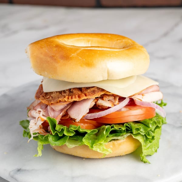 Bagel Nosh bagel sandwich with turkey, bacon, cheese, lettuce, tomato, and red onion.