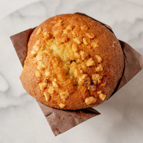 A golden-brown muffin with chopped nuts on top, nestled in a brown paper liner.