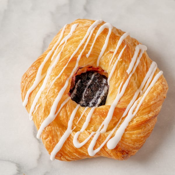 A golden-brown pastry with white icing drizzle and a dark fruit filling in the center.