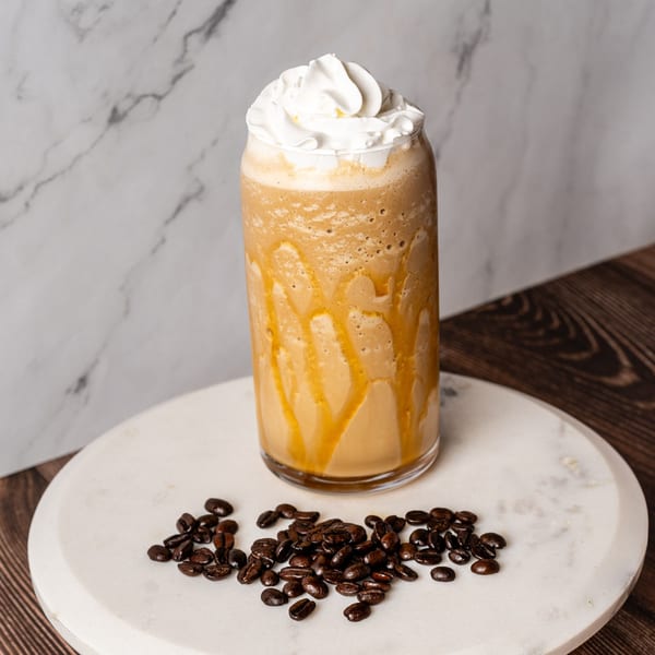 A caramel frappe with whipped cream and coffee beans on a marble tray.