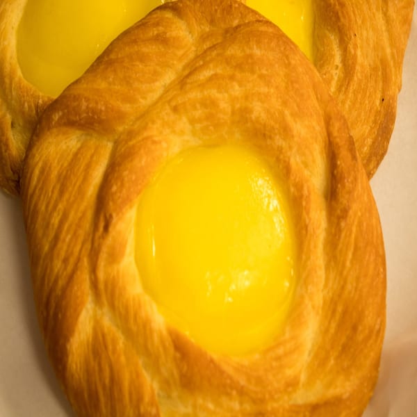 Close-up of a golden-brown pastry with a bright yellow, creamy filling at Bagel Nosh.
