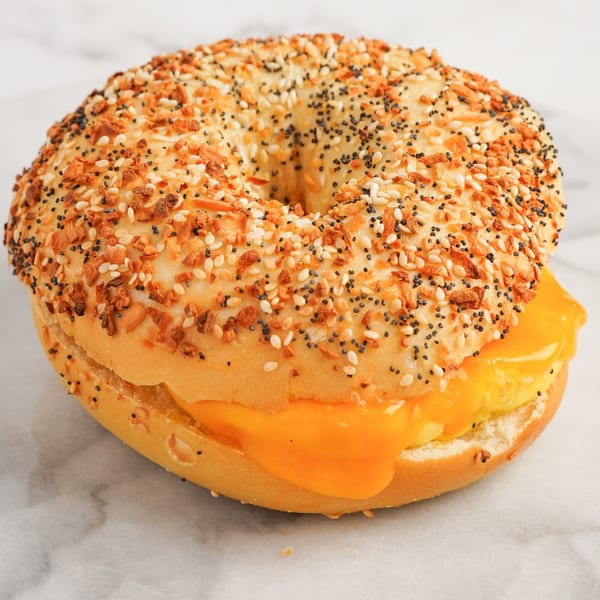 Everything bagel with melted cheese and egg on a white marble surface.