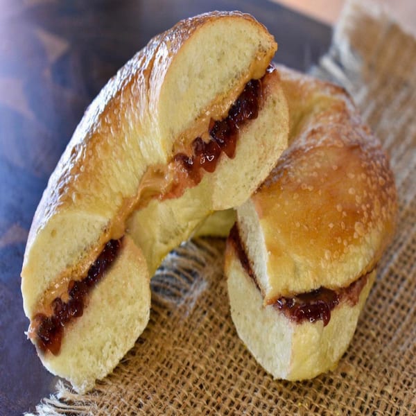 Bagel Nosh bagel sliced in half, filled with peanut butter and jelly, on a burlap surface.