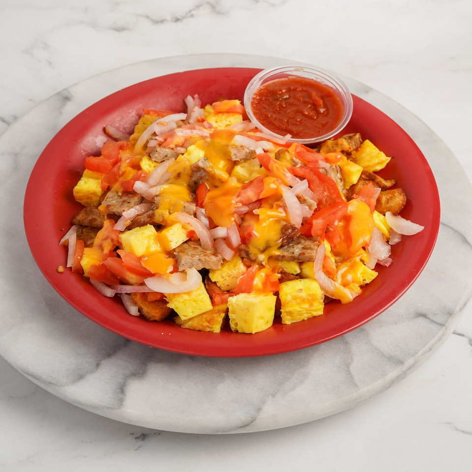 A red plate filled with Bagel Nosh's breakfast scramble, topped with cheese, tomatoes, onions, and salsa.