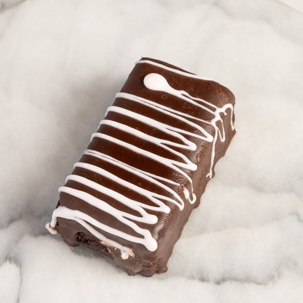 A chocolate brownie bar with white icing drizzle on a white marble surface.